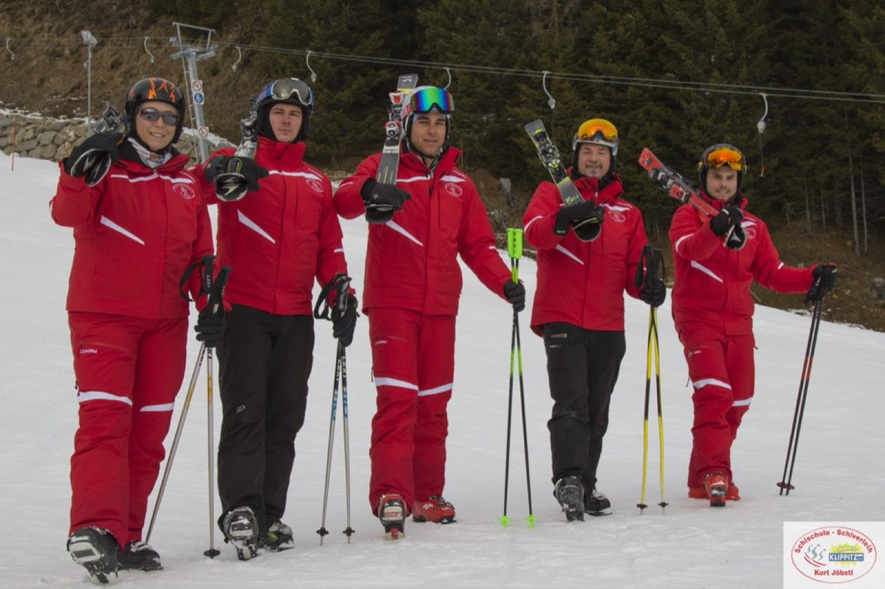 Fünf Skilehrer in roten Anzügen auf der Piste