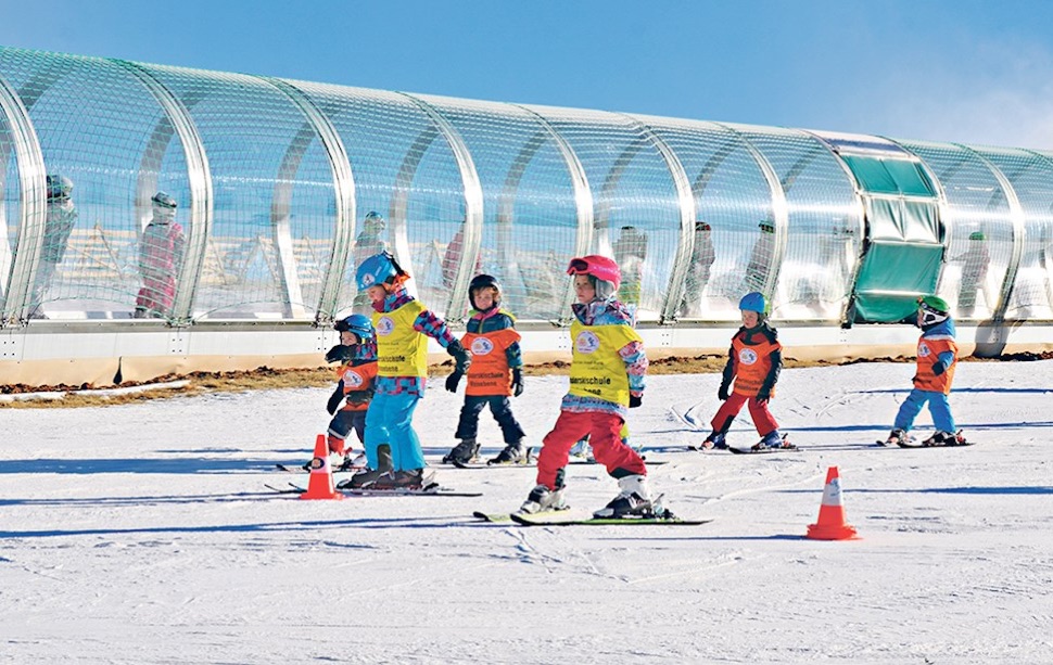 Kinder auf Ski vor dem überdachten Förderband