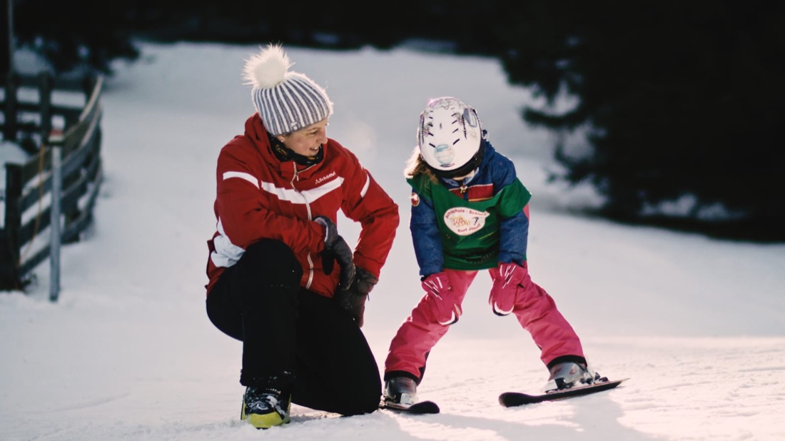 Skilehrerin begleitet ein Kind bei den ersten Schwüngen