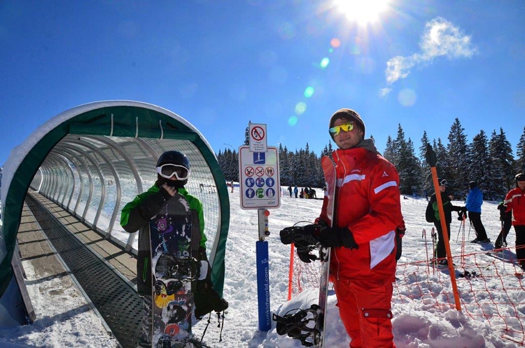 Skilehrer und Kind mit Snowboard am Eingang des Zauberteppichs